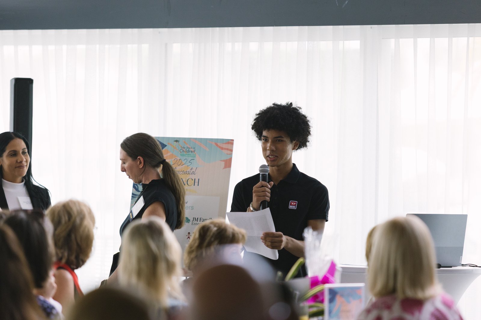 A young man speaking from notes to a seated audience at a Take Stock in Children event
